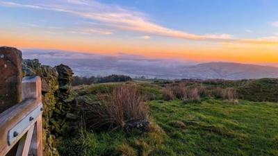 An orange and blue sky with a green field in the foreground