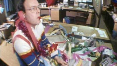 John Mountford looking unenthused sitting on a desk after the office Christmas party.