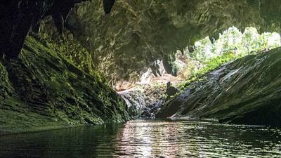 A photo of Tum Luang cave at Doi Nang Non mountain in Chiangrai Province , Mae Sai District , Thailand. The camera looks across dark water to the entrance of the cave.