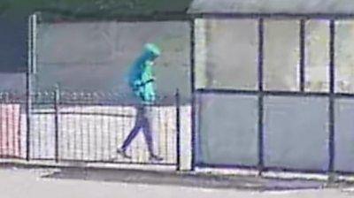 Axel Rudakubana, in a green hoodie and blue face mask, walks on a street near a bus stop