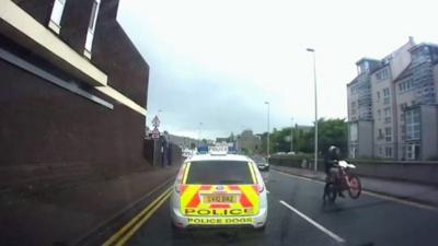 A motorbike does a wheelie while passing a police car