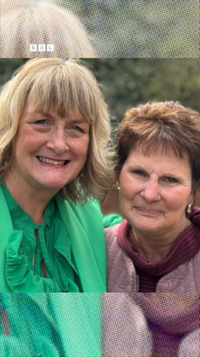 A woman with blonde hair and a green top with a woman who has brown hair and is wearing a pink and purple top