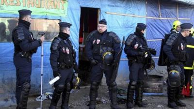 French riot police officers stand at the entrance of the Calais migrant camp, northern France Thursday, Jan.21, 2016.