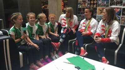 Three Team GB hockey players and four young hockey players sit with each other.