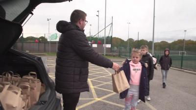 Man handing out lunch bag to child