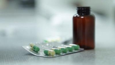 Brown pill bottle with blister pack of green and yellow pill capsules next to it