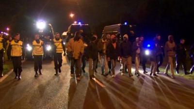 Gendarmes march behind a line of migrants