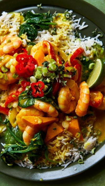A top-down view of prawns, rice and chilis on a dark-coloured plate.