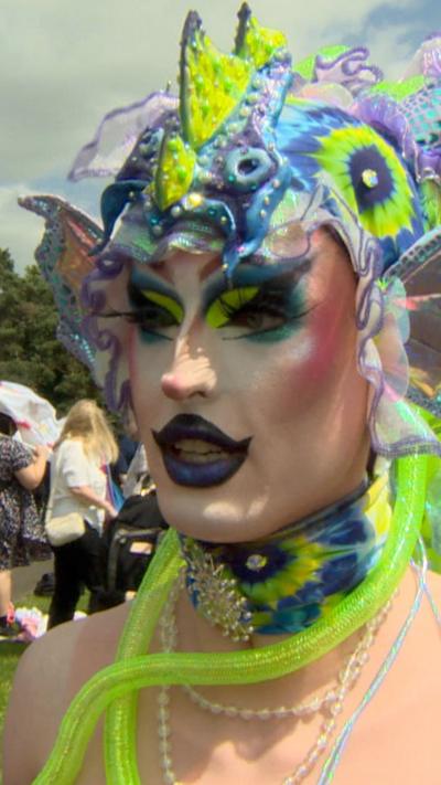 A drag queen wearing green and purple dressed like a dragon