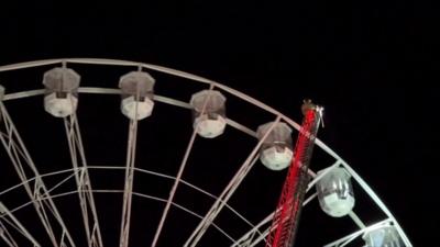 A firefighter climbs a ladder to reach a stalled Ferris wheel.