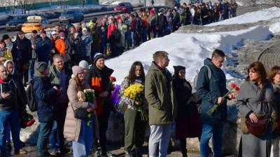 People holding flowers stand in a long queue