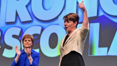 Leanne Wood gives a thumbs up on stage, applauded by Nicola Sturgeon