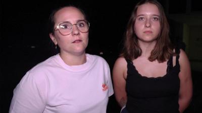 A woman in a pink t-shirt and glasses and other in a black vest.
