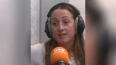 Natalie Cassidy in a radio studio wearing headphones. She has long brown hair.