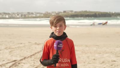 Child Max looking at camera stood on a beach.