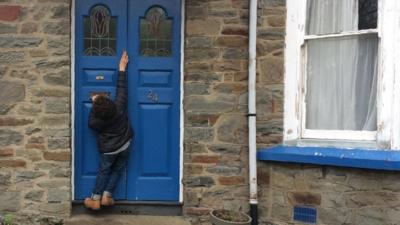 A teenager with dwarfism struggling to reach his front door lock