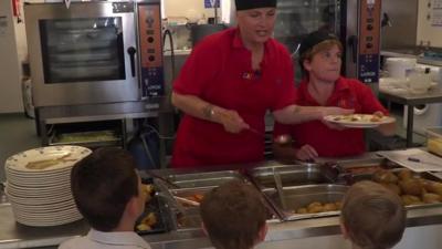 School caterers serving food to three pupils