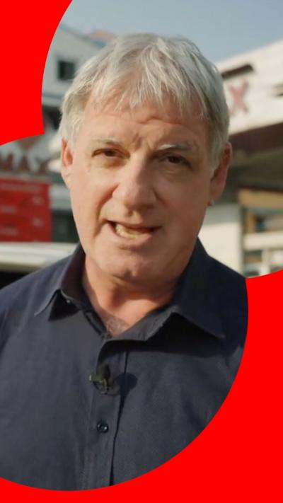 BBC correspondent walking next to queue of vehicles in Myanmar