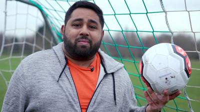 BBC Click reporter Omar Mehtab stands in a goal while holding a football