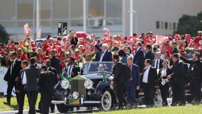 Lula waves at crowds from an open-topped car in Brazil.