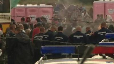 Hungarian police standing in a line in front of a group of migrants protesting at a reception camp on the Hungarian border with Serbia (after tear gas has been fired)