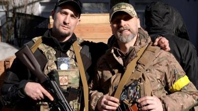 Men with guns, one wearing military fatigues, one black