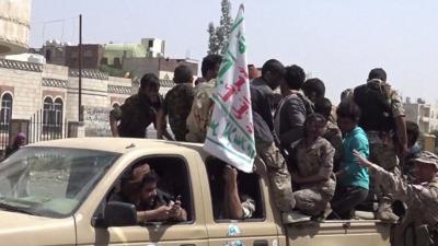 Houthi fighters clamber on the back of a pickup truck