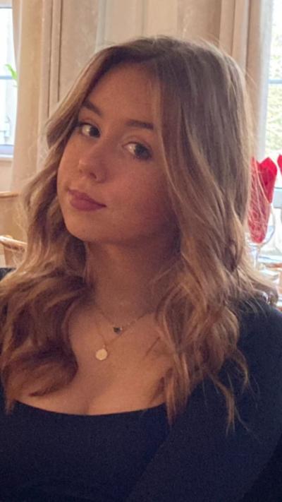 Jessica Glasser sitting at a table. She is wearing a long sleeve black top and gold necklaces. She has long, waved blonde hair and is smiling at the camera.