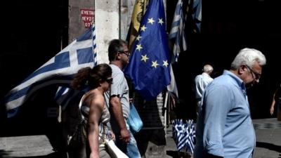 People walk past Greek and WU flags in Athens