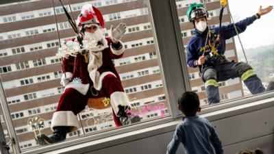 Santa and his helper wave to a child while abseiling down a hospital in Barcelona, 21 December 2021