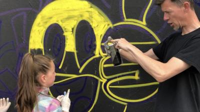 man teaching girl how to use spray paint can