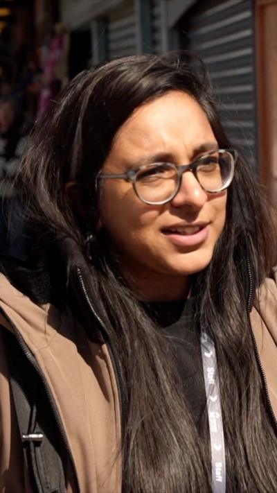 A woman with dark hair and spectacles wears a black jacket and looks at the camera.