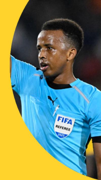 A picture of Omar Abdulkadir Artan dressed in a light blue uniform, appearing to have his hand raised while refereeing a game 
