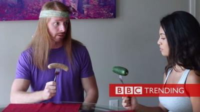 Image from video 'If Meat Eaters Acted Like Vegans'. Man holding sausage, woman holding cucumber.