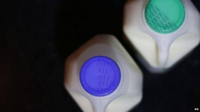 Close up looking down on two plastic milk cartons, one with a blue lid, one with a green lid