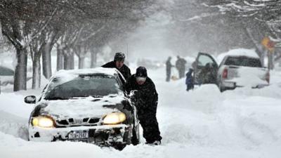 Two men trying to push a car in a snow covered street