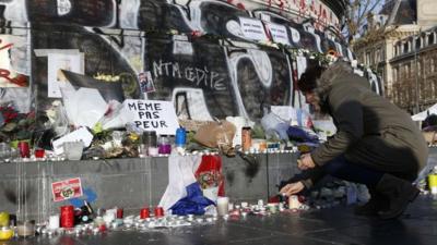 People lighting candles at a memorial in Paris