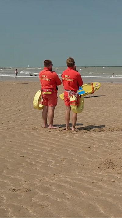 Two lifeguards on a sandy beach holding boards