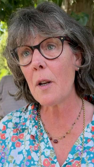 woman with grey hair and black glasses wearing a blue flowery top