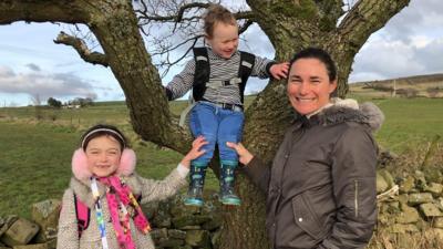 paralympian-sarah-storey-stands-next-to-a-tree-with-her-young-children-beside-her