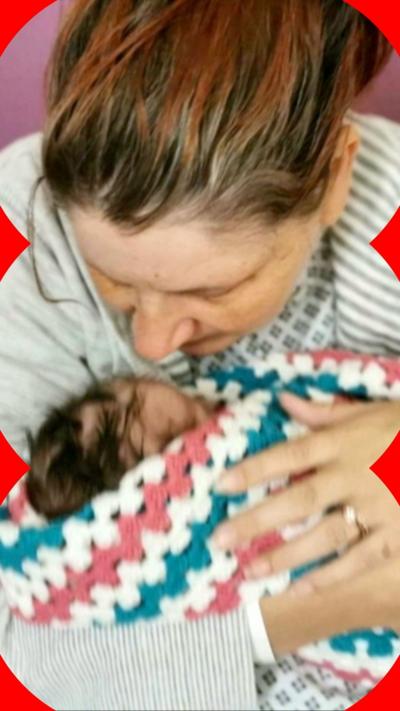 A woman holds a baby wrapped in a colourful knitted blanket