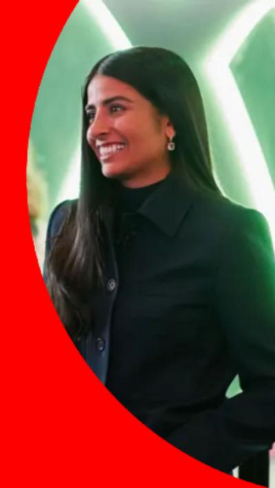A woman with long dark hair dressed in all black is smiling while chatting to another woman with short red hair dressed in green.