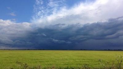 Shower clouds build over a green field.
