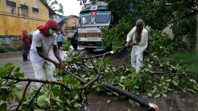 Rescue workers cut tree branches that fell on a truck trailer after heavy winds caused by Cyclone Amphan, in Kolkata