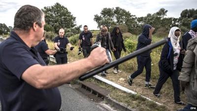 French police officers escort migrants who were waiting alongside a road near the Eurostar train tracks in Coquelles on the outskirts of Calais - 3 August 2015