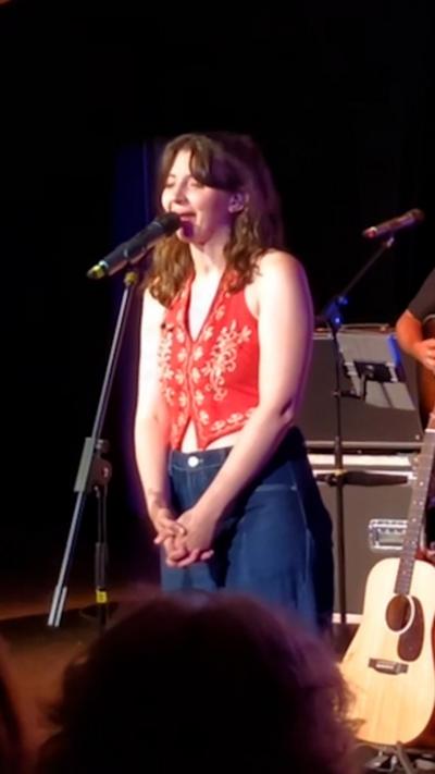 Hannah Richards - young woman wearing a red top and jeans, speaking into a microphone on stage