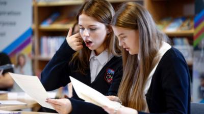Two teenage girls in school uniforms looking surprised opening their results