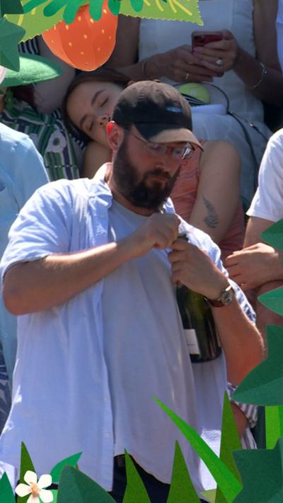 Man in crowd struggles to open champagne bottle