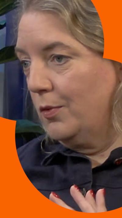 A woman with wavy hair and a dark coloured shirt looks at someone off camera