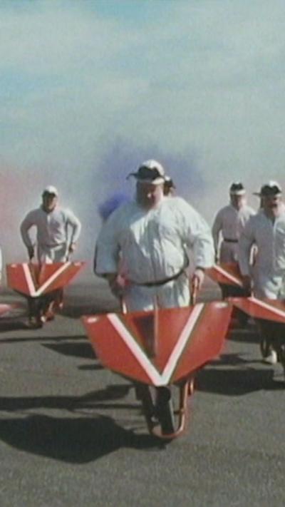 Men in white boiler suits pushing red wheelbarrows